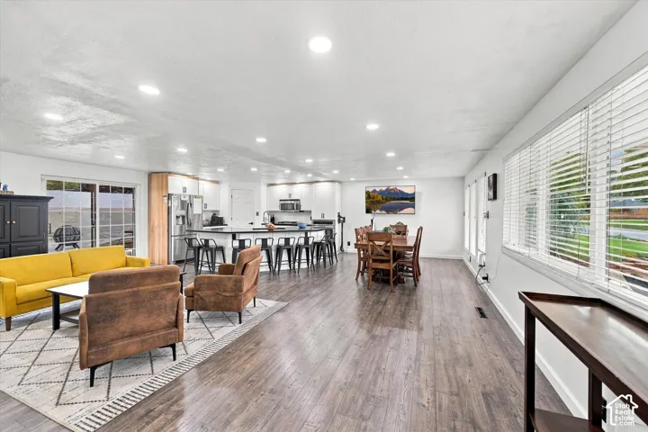 Open-concept area featuring wood-finish flooring, recessed lighting, white cabinetry, a curved island with countertop seating, and sliding glass doors
