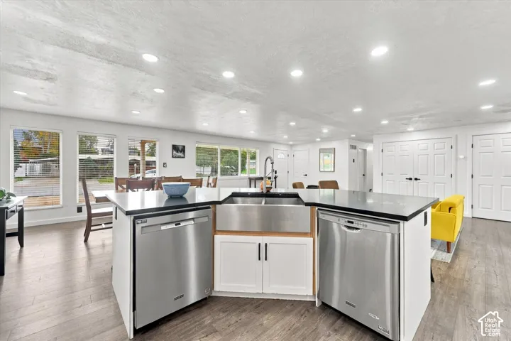 Kitchen island featuring dual stainless steel dishwashers, an undermount farmhouse sink, dark countertops, recessed lighting, and wood-finish flooring