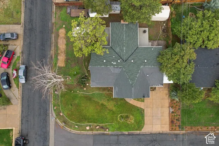 Aerial perspective of a corner lot property featuring a multi-gable shingle roof, paved driveway, concrete walkway, and mature trees