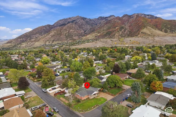 Aerial perspective of a single-story residence with a brick exterior, prominent mountain backdrop, mature trees, and established landscaping
