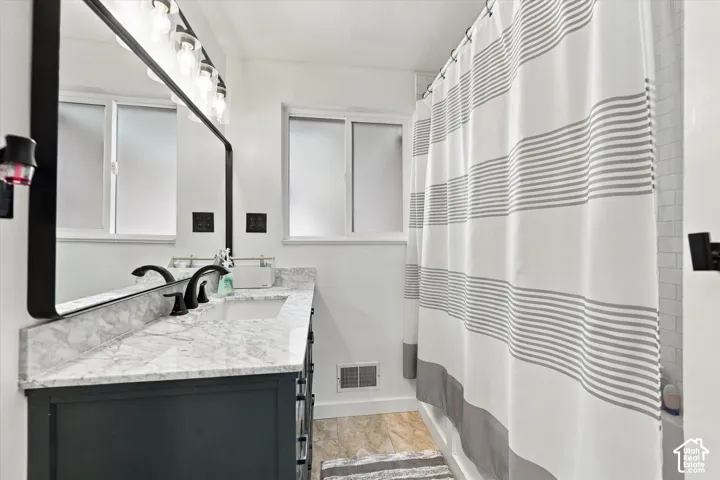 Dark-finish vanity with stone-pattern countertop, rectangular undermount sink, matte black faucet, full-width mirror with black frame, and multi-bulb industrial-style vanity light