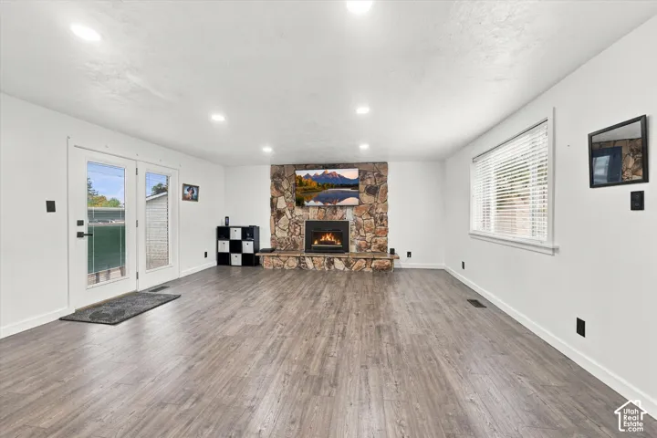 Living area featuring wood-finish flooring, stone-veneer fireplace with a raised hearth, recessed lighting, and double glass-pane doors