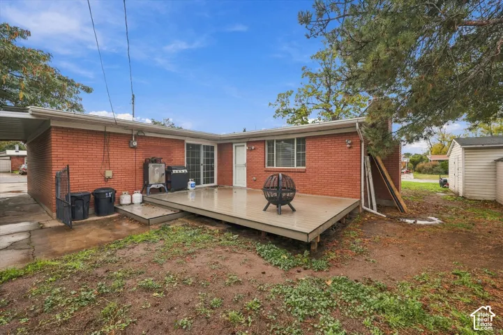 Rear exterior featuring red brick masonry, a raised composite deck, a covered carport, and a detached storage shed