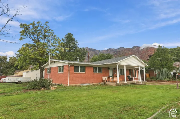 Ranch-style brick exterior featuring a covered front porch with columns, gabled roofline, and mountain backdrop
