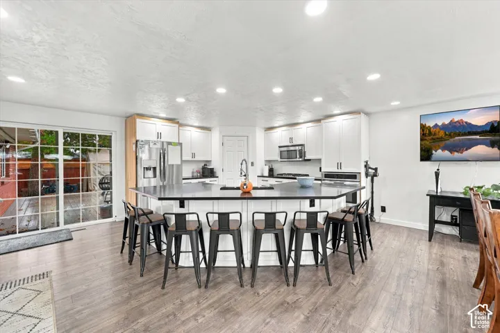 Kitchen featuring white shaker-style cabinetry, a large peninsula with a dark countertop, recessed lighting, and wood-finish flooring