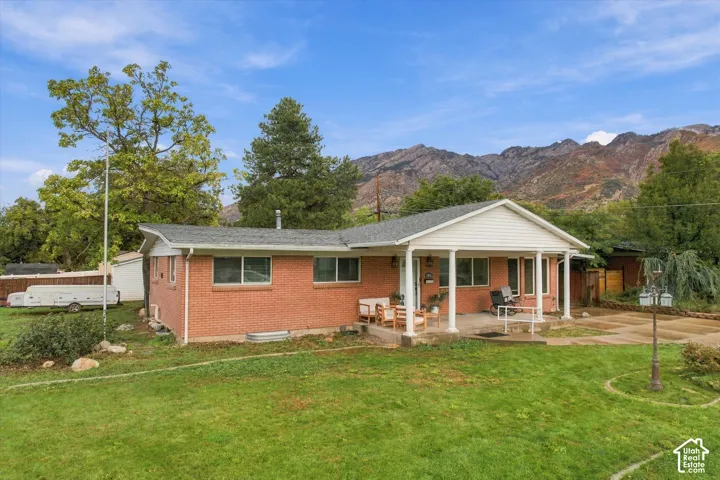 Single-story brick exterior featuring a covered front porch with columns, a concrete driveway, and a mountain backdrop