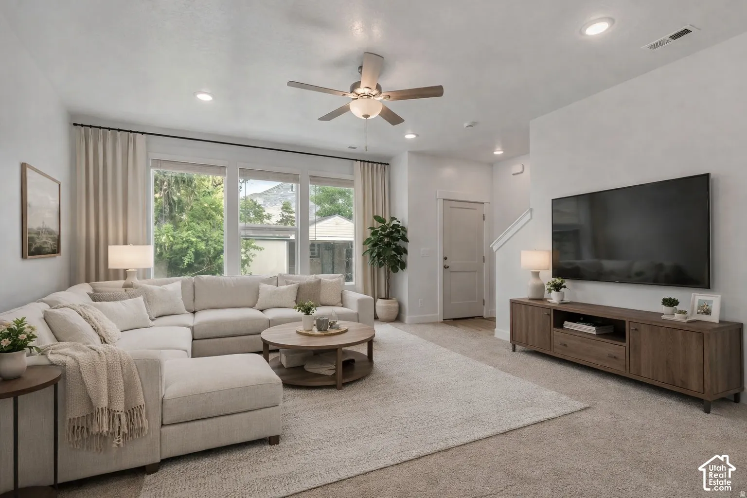 Living area featuring neutral wall-to-wall carpeting, recessed ceiling lighting, a multi-blade ceiling fan with an integrated light fixture, and large multi-pane windows