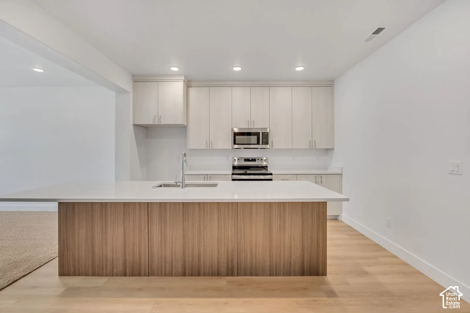 Kitchen featuring light-toned cabinetry, a wood-finish island, solid-surface countertops, recessed lighting, and stainless steel appliances