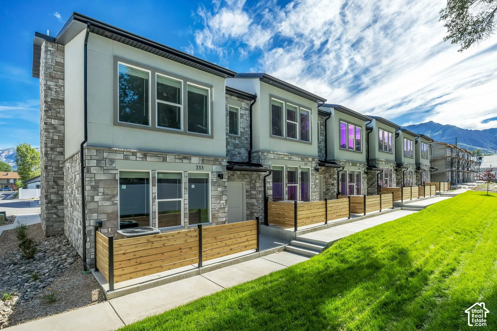 Multi-unit exterior featuring stone veneer siding, dual-pane windows, wood-finish privacy partitions, concrete walkways, and mountain scenery