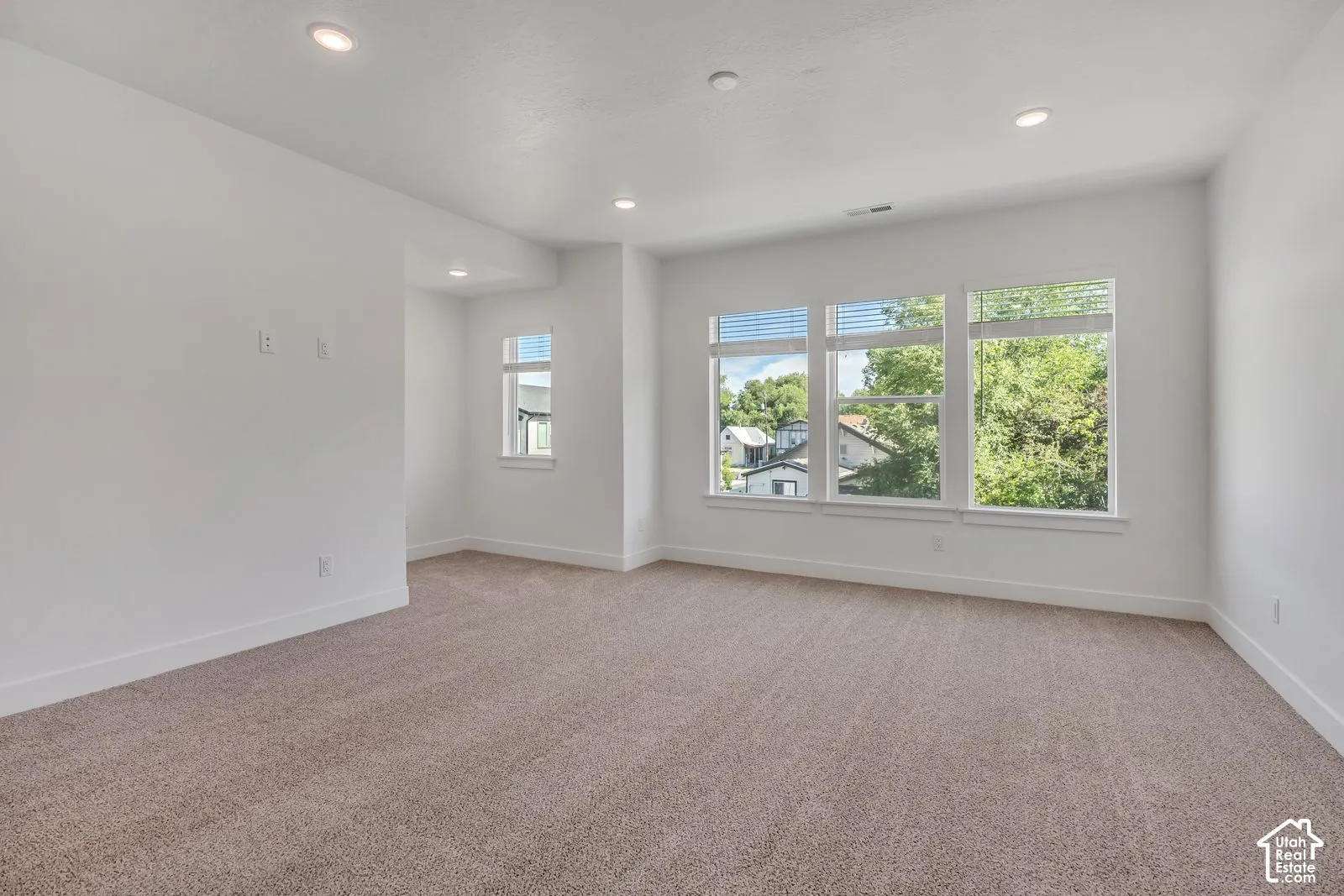 Neutral-toned wall-to-wall carpeting, recessed ceiling lighting, and large windows with horizontal blinds