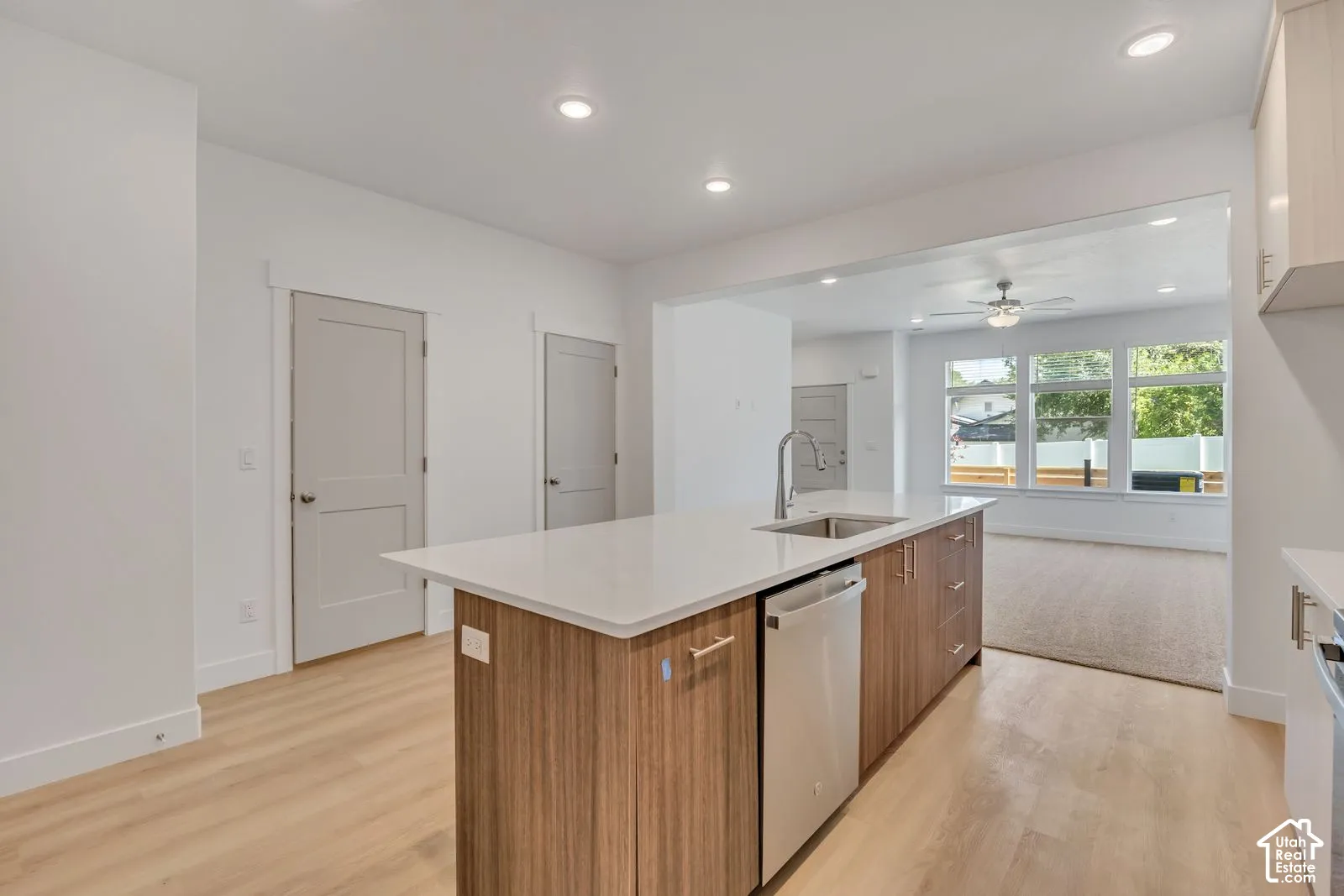 Kitchen island featuring stone countertops, integrated stainless steel dishwasher, undermount sink with gooseneck faucet, and wood-finish cabinetry, set against wood-finish flooring and recessed lighting