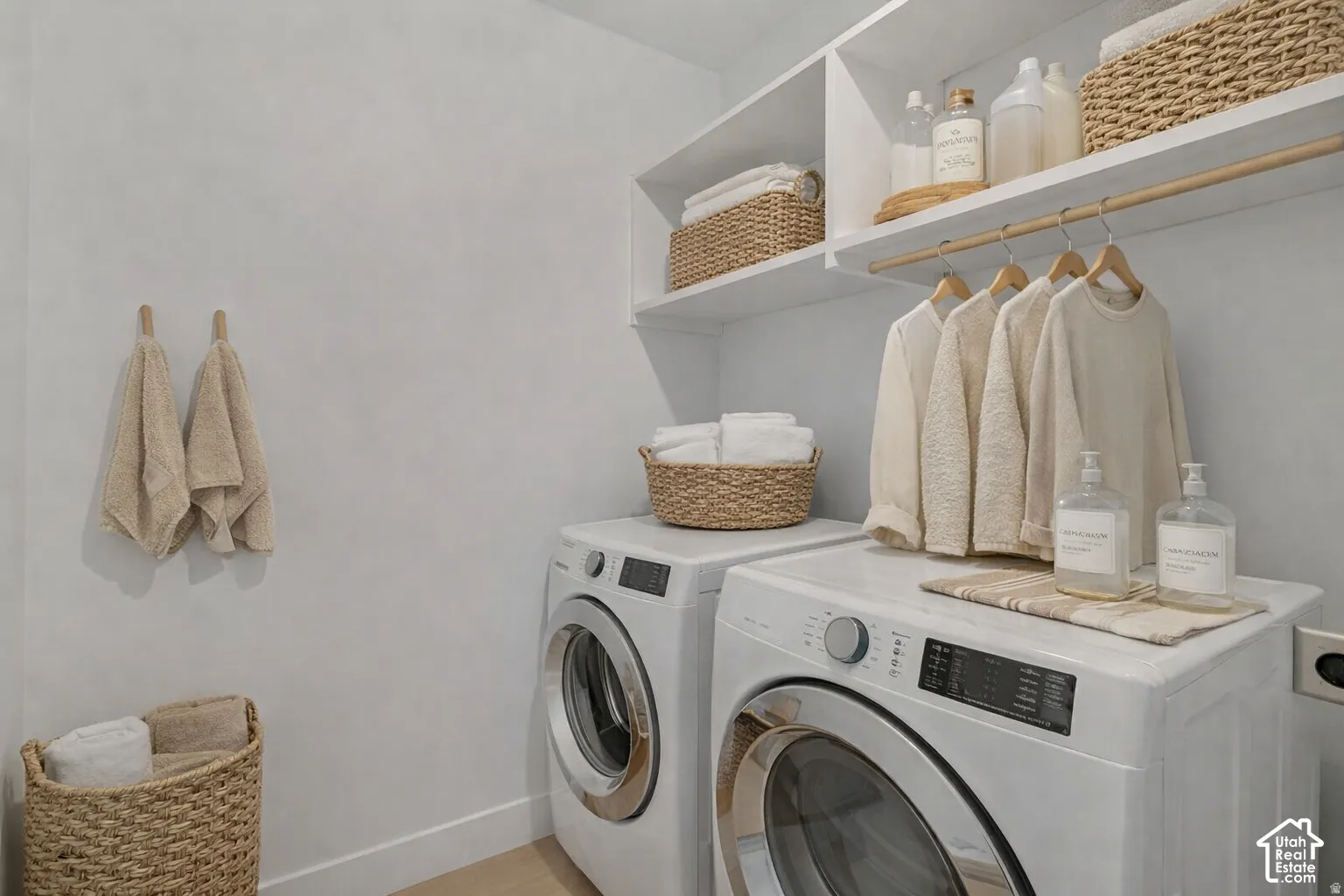 Laundry room featuring white front-load washer and dryer, custom built-in upper shelving, and a natural wood-finish hanging rod