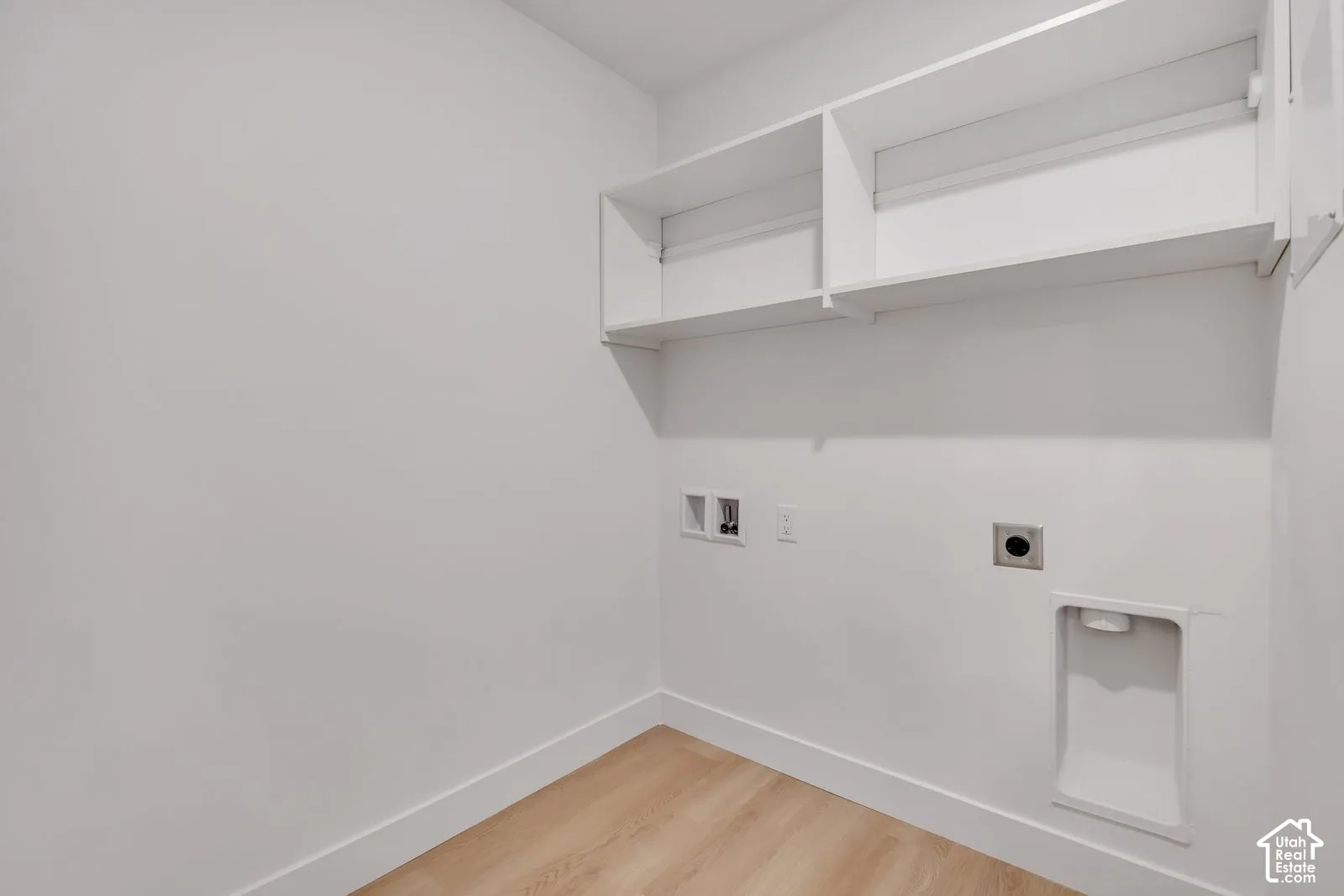 Utility area featuring white walls, light-toned wood-finish flooring, built-in overhead shelving, and dedicated hookups for laundry appliances