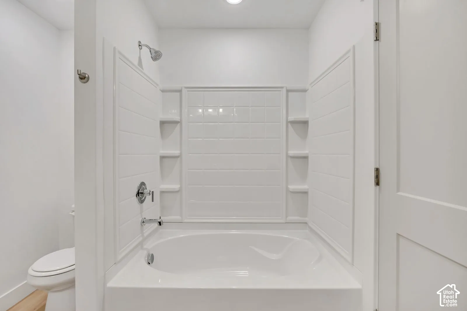 Soaking tub with integrated tile-patterned surround, built-in shelving, chrome fixtures, and a dual-flush toilet
