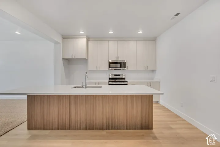 Kitchen featuring light-toned cabinetry, a wood-finish island, solid-surface countertops, recessed lighting, and stainless steel appliances