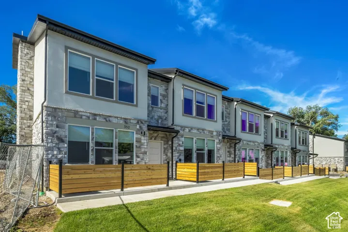 Multi-family exterior featuring light-toned stone veneer, smooth stucco siding, horizontal wood-slat privacy fencing, and concrete patios