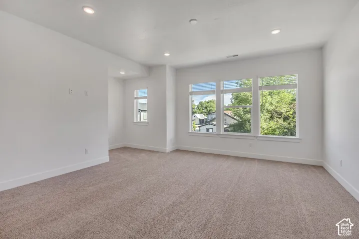 Neutral-toned wall-to-wall carpeting, recessed ceiling lighting, and large windows with horizontal blinds