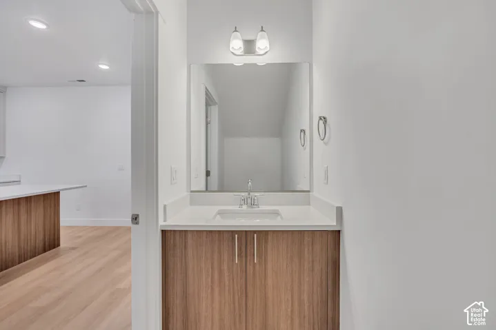 Wood-finish vanity with a rectangular undermount sink, solid-surface countertop, full-width mirror, and two-light wall fixture