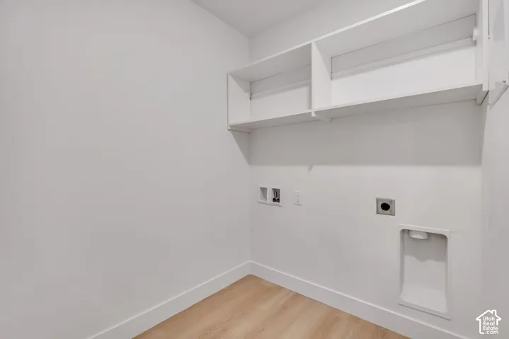 Utility area featuring white walls, light-toned wood-finish flooring, built-in overhead shelving, and dedicated hookups for laundry appliances