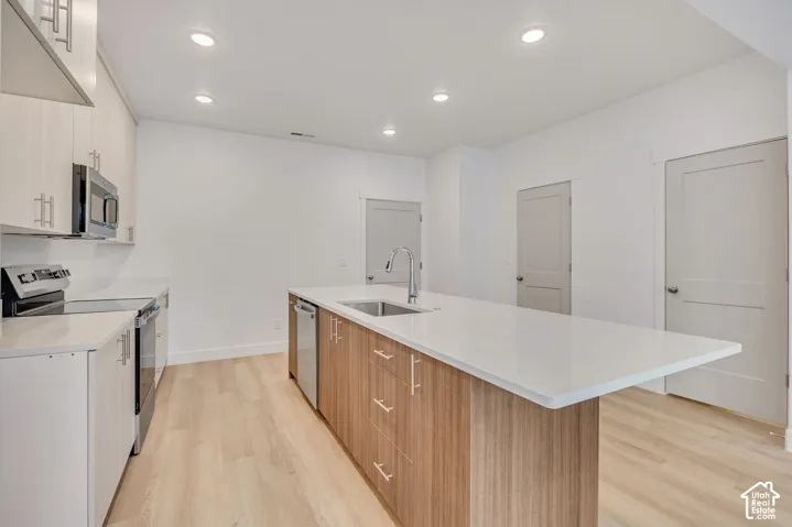 Kitchen featuring a central island with a solid-surface countertop, stainless steel undermount sink, light wood-finish cabinetry, wood-finish flooring, and recessed ceiling lighting