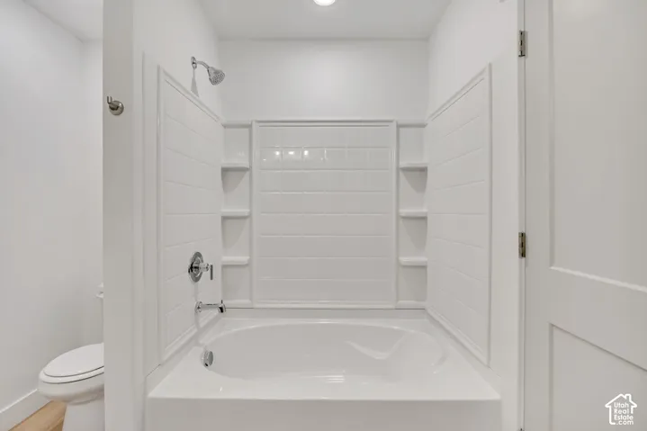 Soaking tub with integrated tile-patterned surround, built-in shelving, chrome fixtures, and a dual-flush toilet