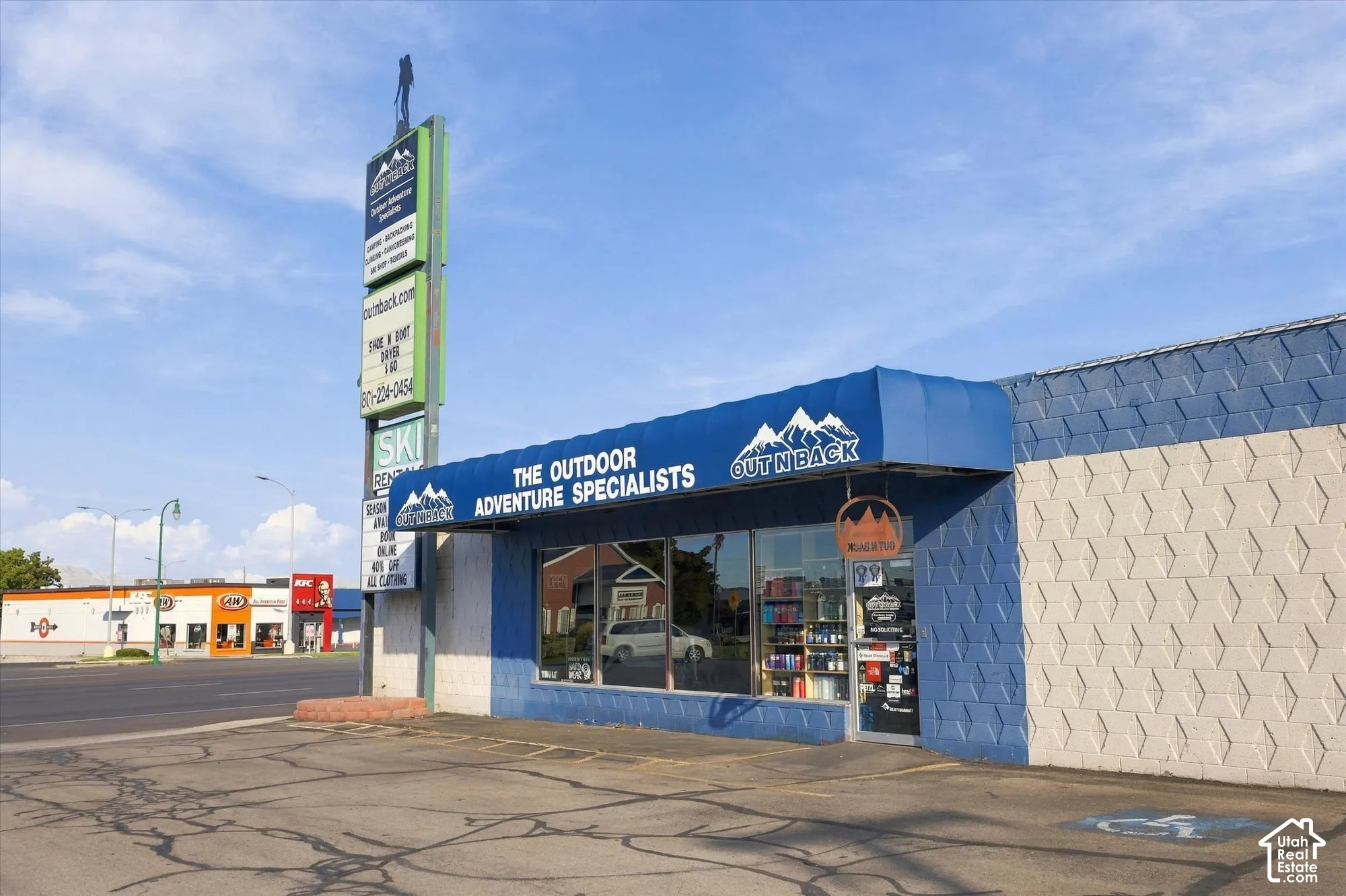 Commercial storefront featuring a patterned concrete masonry exterior, expansive glass display windows, a prominent blue metal awning, and a dedicated pylon signage structure