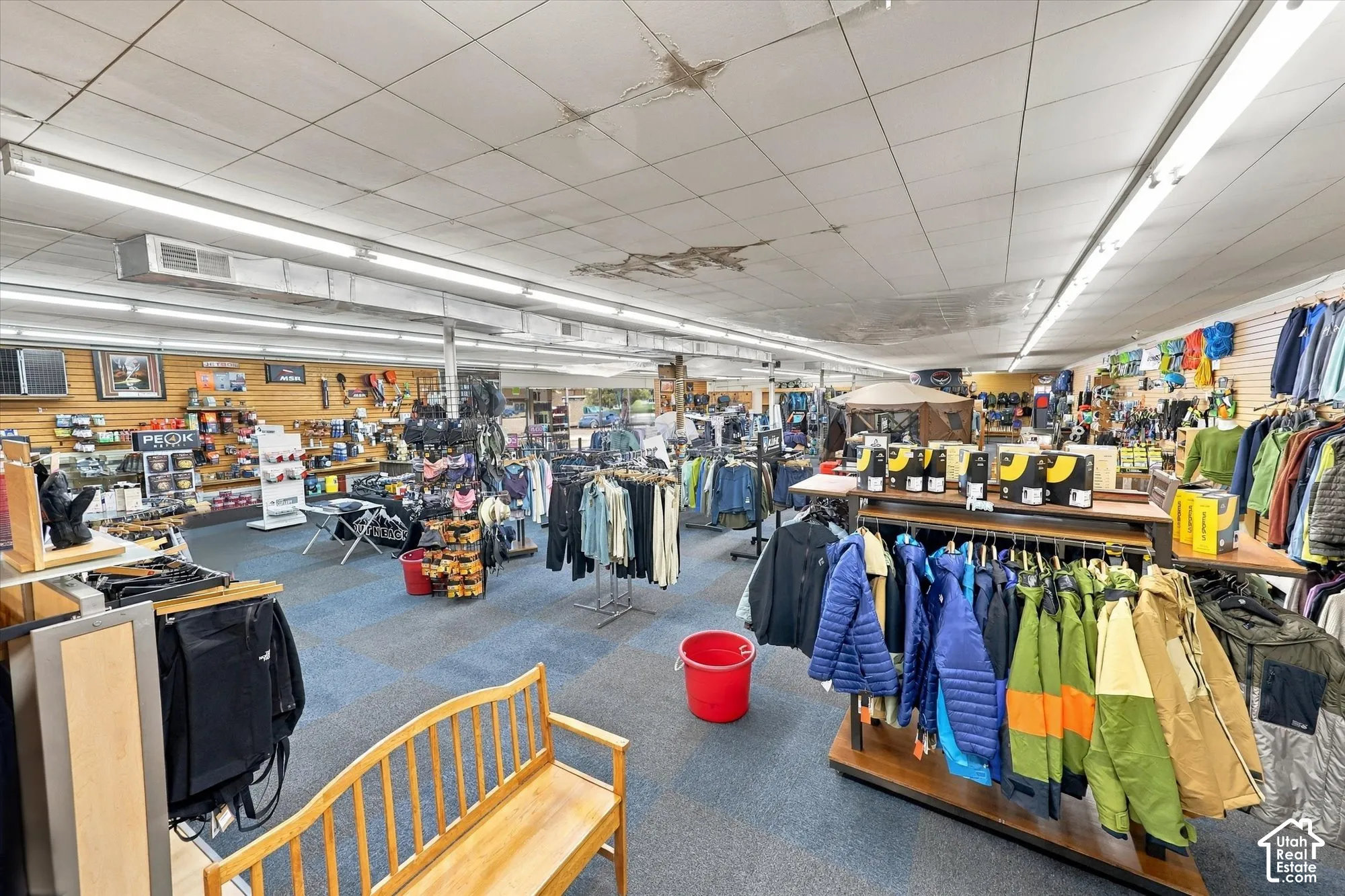 Expansive open-concept commercial space featuring modular slatwall paneling, linear fluorescent overhead lighting, exposed structural ductwork, and commercial-grade carpeting