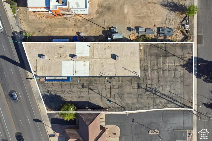 Aerial perspective of the property highlighting an expansive asphalt parking area and a flat-roof structure equipped with roof-mounted HVAC units