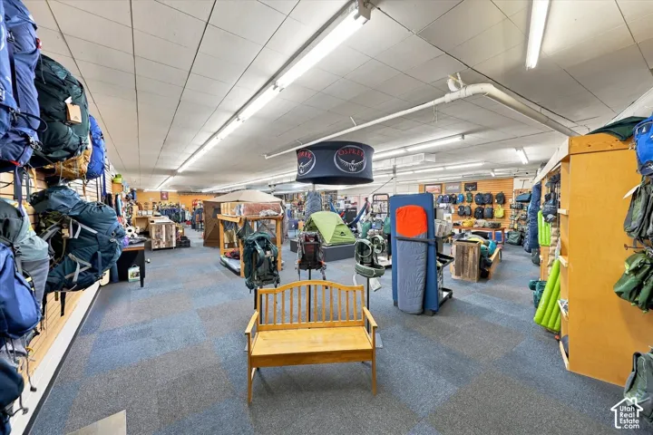 Commercial space featuring carpeted flooring, drop ceiling panels, linear fluorescent lighting, and modular wall-mounted slat board display systems
