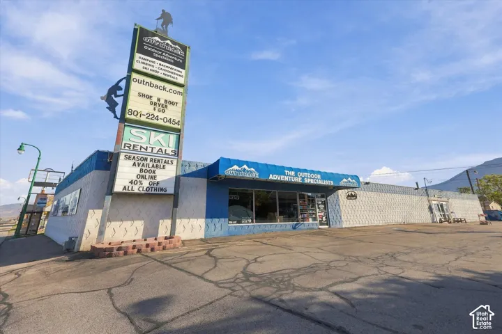 Commercial property featuring a prominent pylon signage structure, expansive glass storefront windows, a metal awning, patterned masonry exterior, and a paved parking area