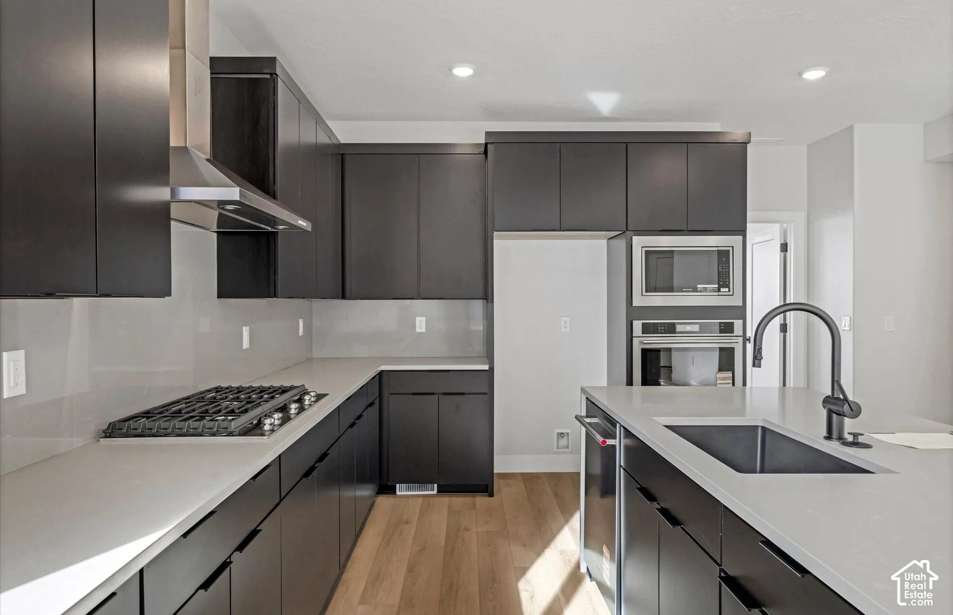 Kitchen featuring dark cabinetry, solid-surface countertops, wood-finish flooring, built-in stainless steel appliances, and a matte black faucet