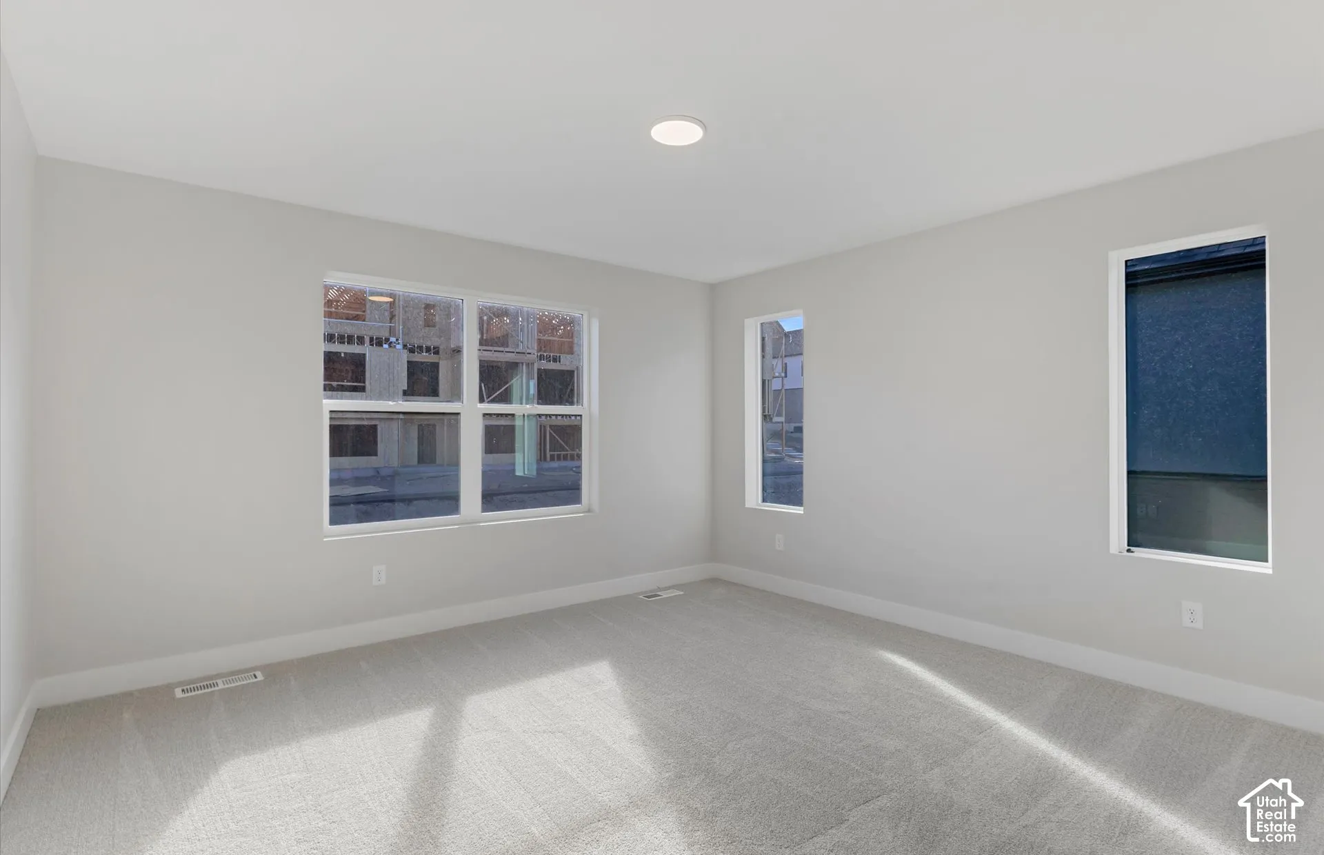 Neutral-toned interior space featuring light-colored wall-to-wall carpeting, multiple windows, and recessed ceiling lighting