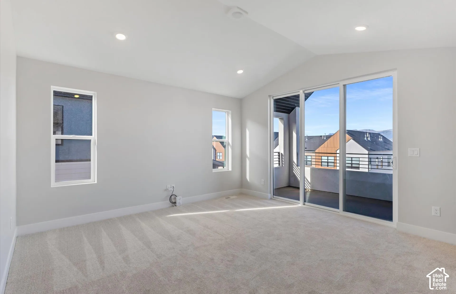 Vaulted ceilings, neutral carpeting, recessed lighting, and large sliding glass doors opening to a covered balcony