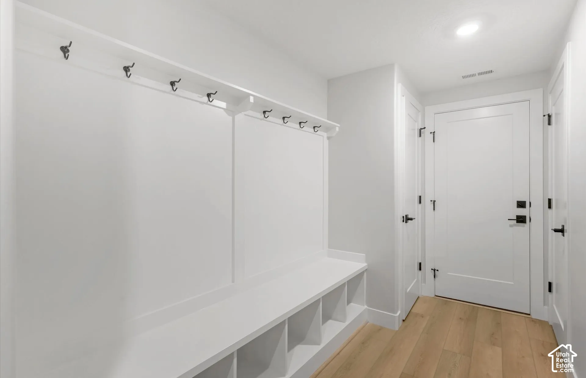 Built-in wall unit featuring a custom bench with open storage cubbies and a full-length coat rack with metal hooks, complemented by wood-finish flooring and solid-core paneled doors with matte black hardware