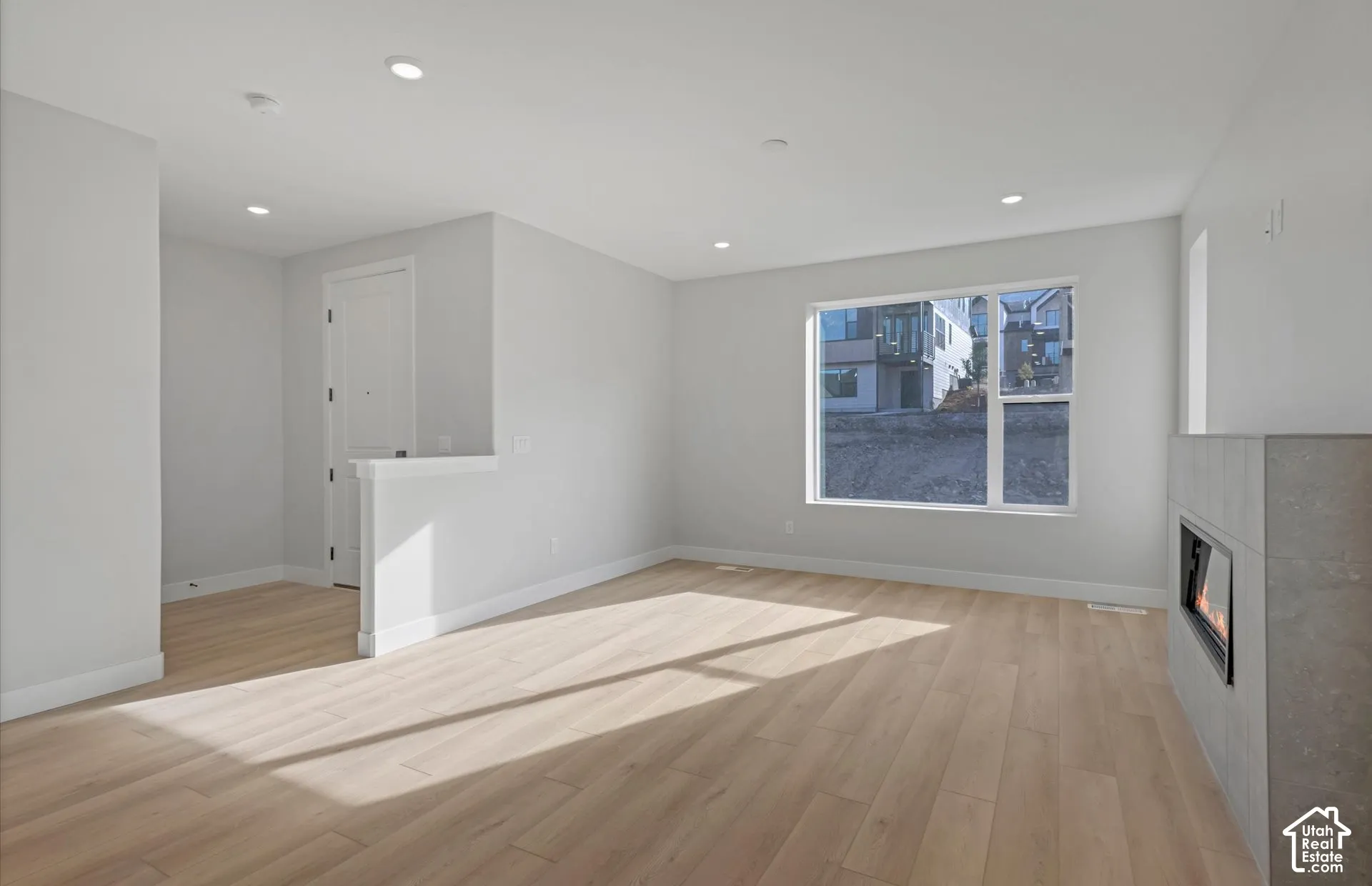 Neutral-toned interior featuring wood-finish flooring, recessed lighting, and a linear fireplace with a concrete-finish surround