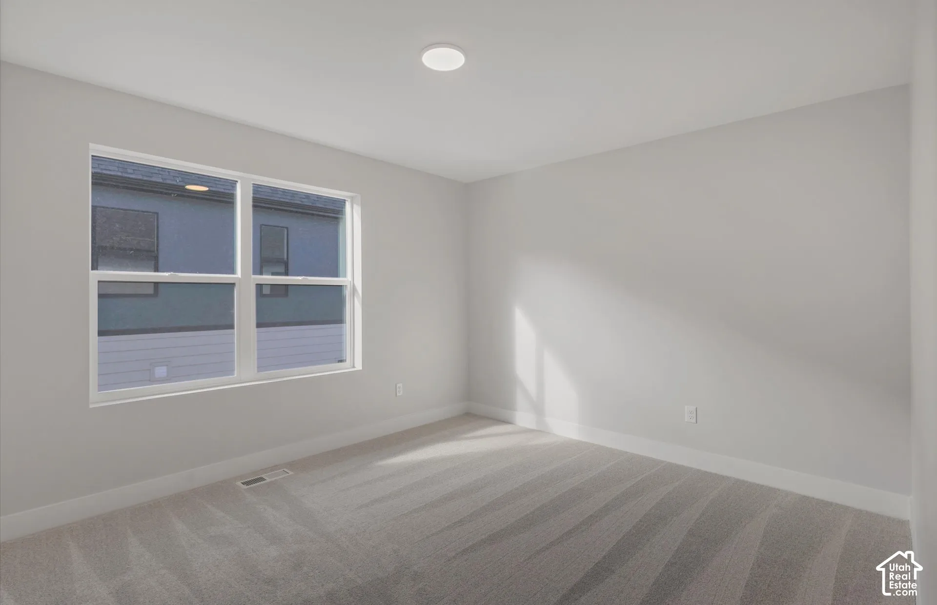 Neutral-toned interior space featuring light-colored wall paint, plush carpeting, a multi-pane window, and a recessed ceiling light