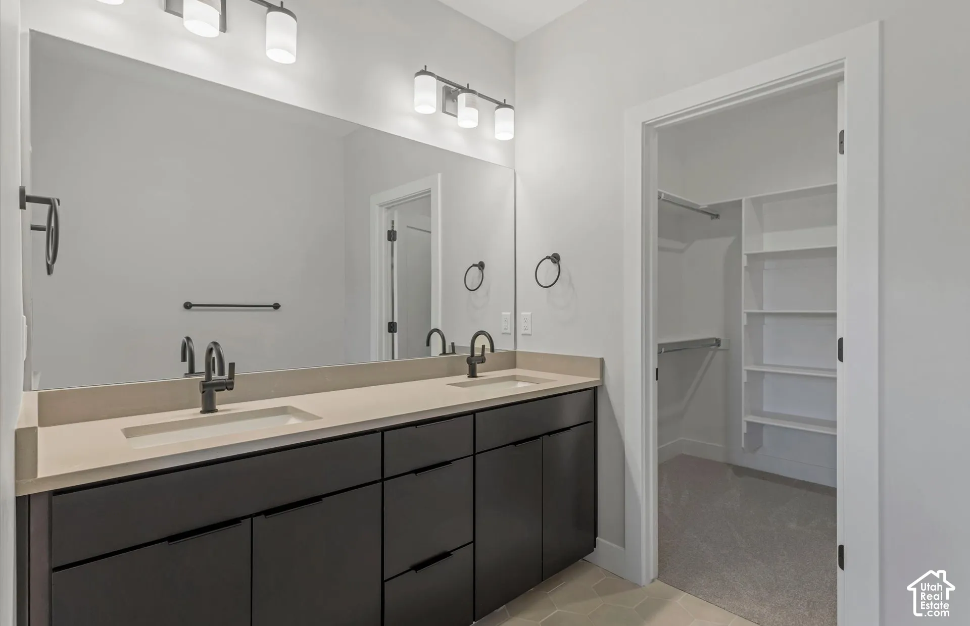 Double vanity featuring a light-toned countertop with dual integrated sinks, matte black faucet hardware, flat-panel dark cabinetry, and dual tri-light wall fixtures