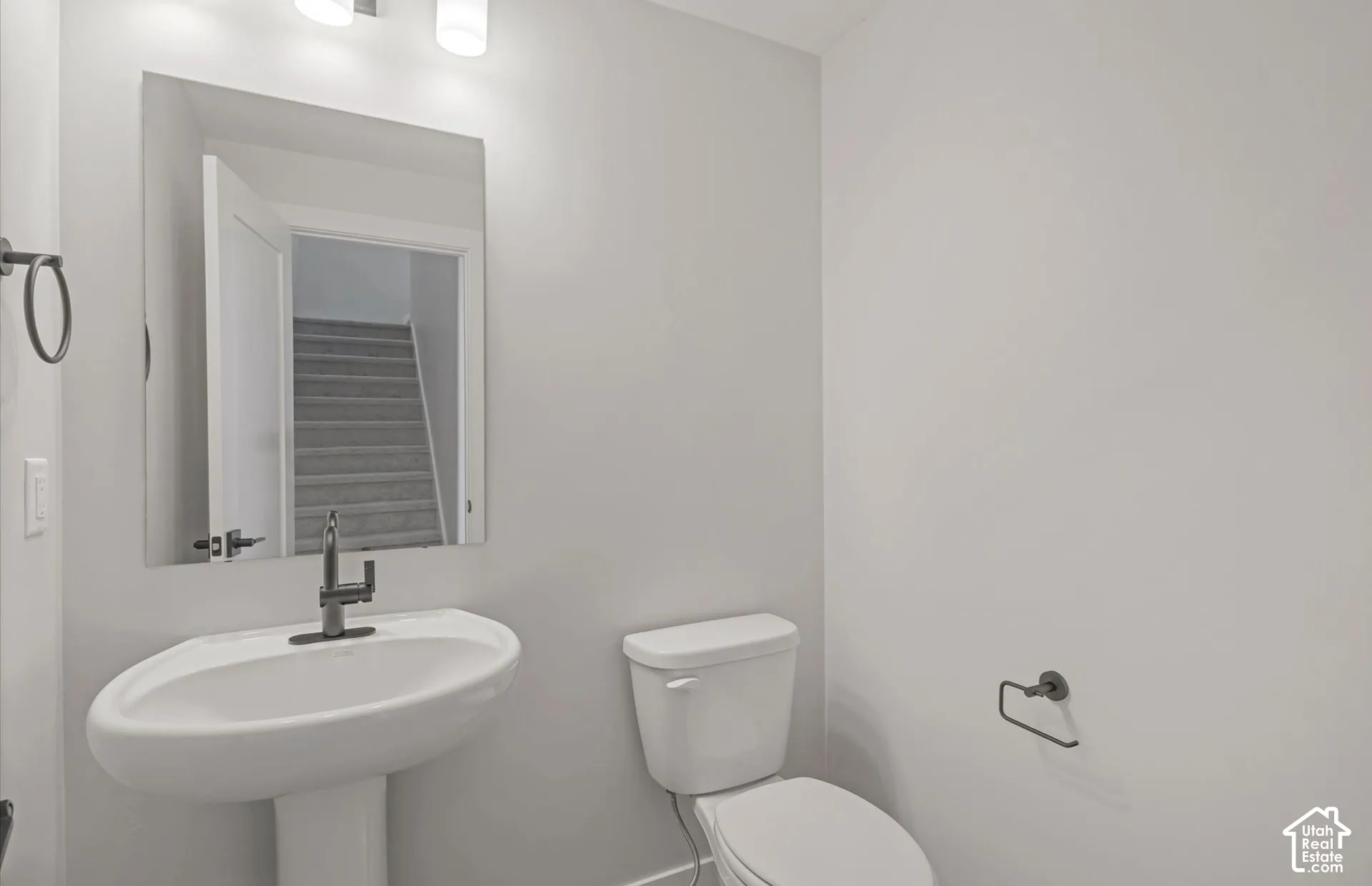 Pedestal sink with a modern metal faucet, wall-mounted mirror, two-light fixture, and matte black hardware