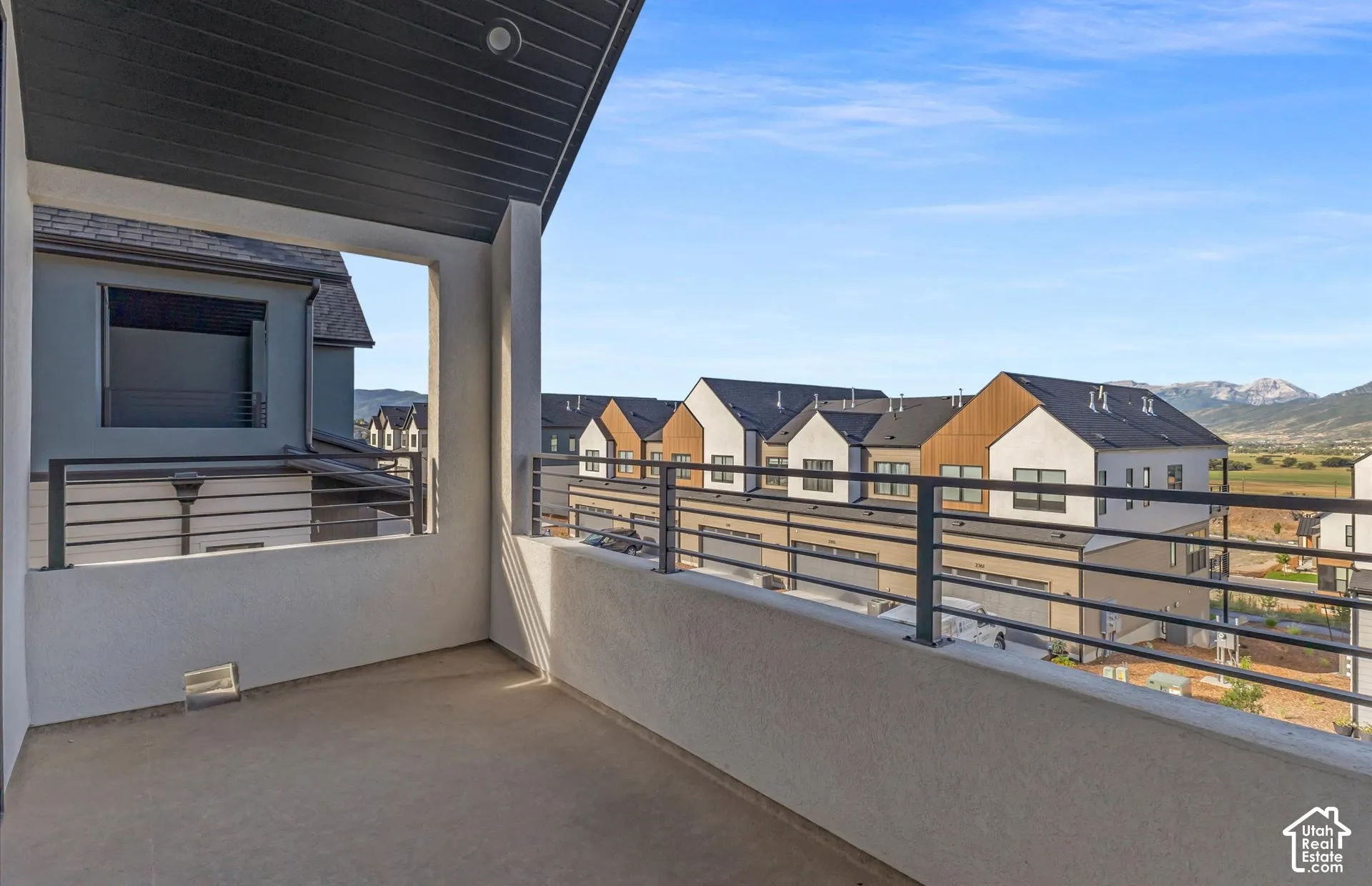 Covered balcony featuring a high-contrast dark wood-finish ceiling, concrete flooring, horizontal metal railing, and mountain backdrop