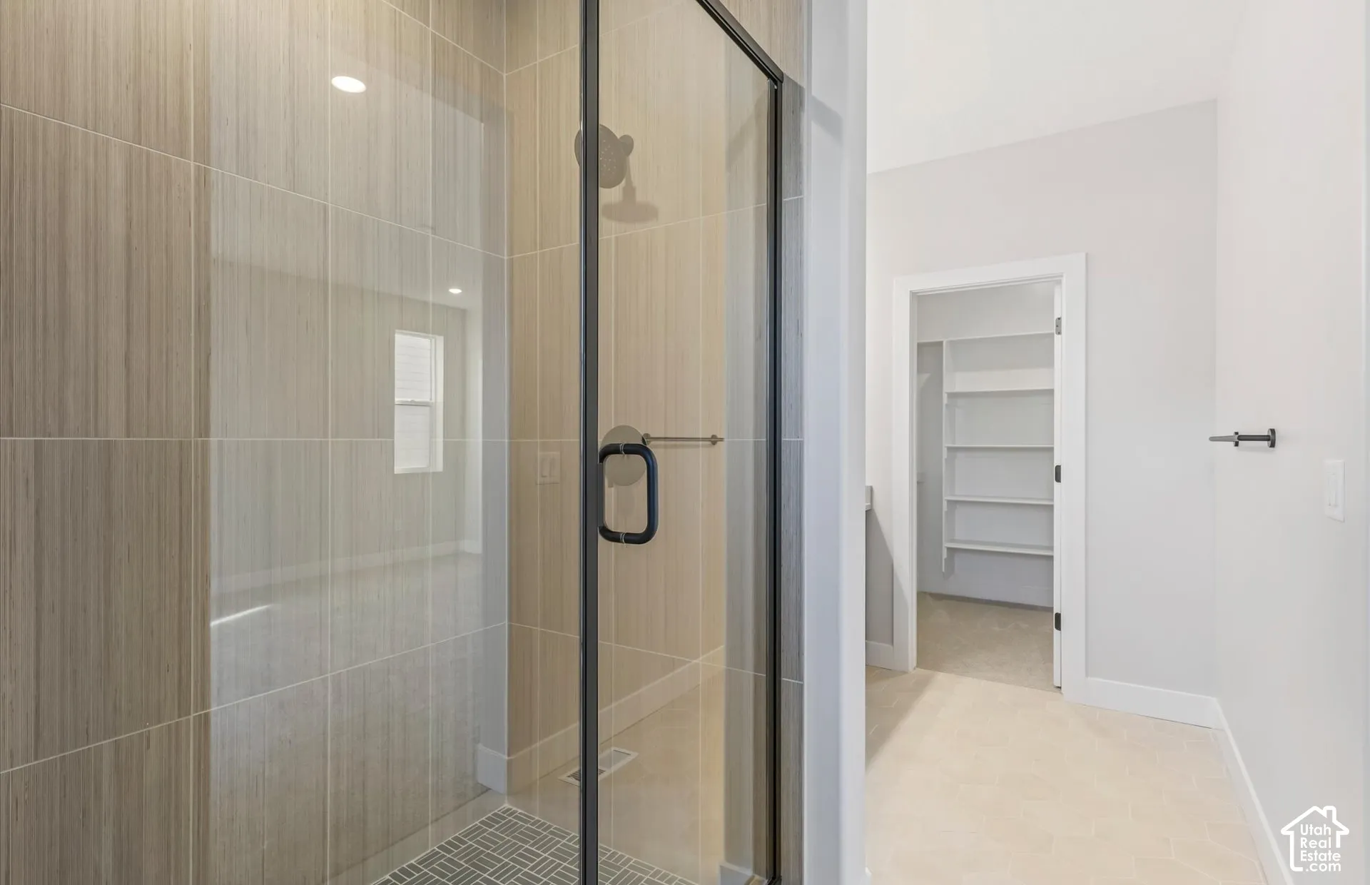 Walk-in shower with vertical tile surround, glass door with matte black hardware, and mosaic tile flooring, featuring a built-in shelving unit in the storage area