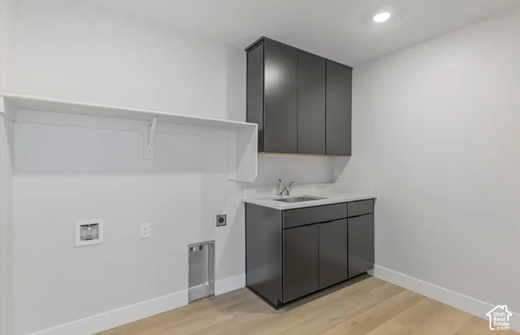 Dedicated room featuring wood-finish flooring, dark-finish cabinetry, an integrated basin, a stone-surface countertop, and an elongated built-in shelf