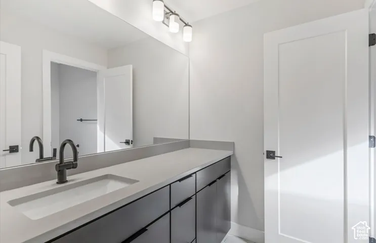 Modern vanity featuring dark cabinetry, a solid-surface countertop with an integrated rectangular sink, matte black faucet, and a wall-to-wall mirror with three-light fixture