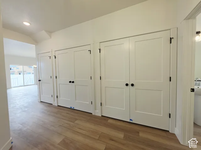 Interior hallway featuring wood-finish flooring, two sets of white two-panel shaker-style closet doors, matte black hardware, and recessed lighting