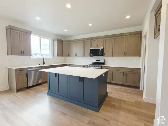 Kitchen featuring wood-finish cabinetry, a contrasting central island, light-toned stone countertops, subway tile backsplash, and stainless steel appliances