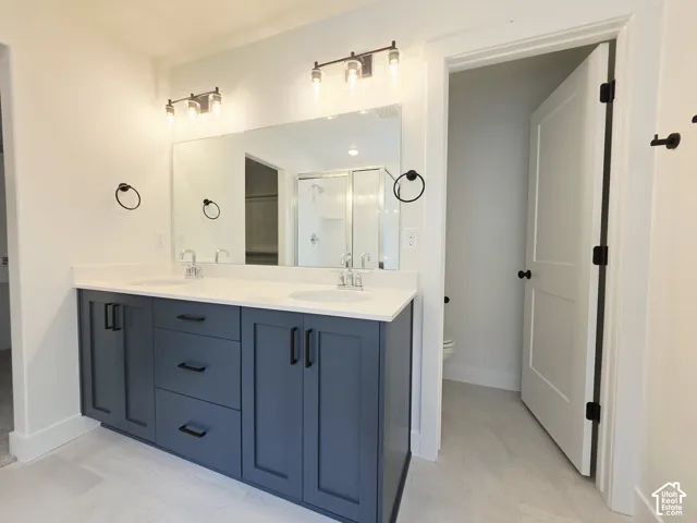 Double vanity featuring dark cabinetry, solid-surface countertops with dual integrated sinks, matte black hardware, and wall-mounted light fixtures