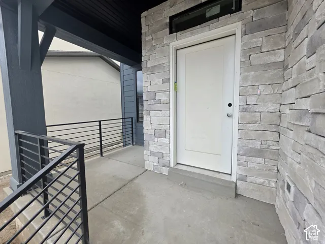 Covered entryway featuring natural stone veneer siding, a solid entry door with transom window, concrete porch flooring, and a modern metal horizontal-bar railing