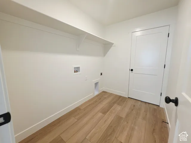 Dedicated utility space featuring wood-finish flooring, a white two-panel interior door with matte black hardware, and an integrated full-length wall shelf