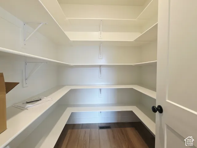 Storage space featuring multiple tiers of white shelving supported by bracket mounts and wood-finish flooring