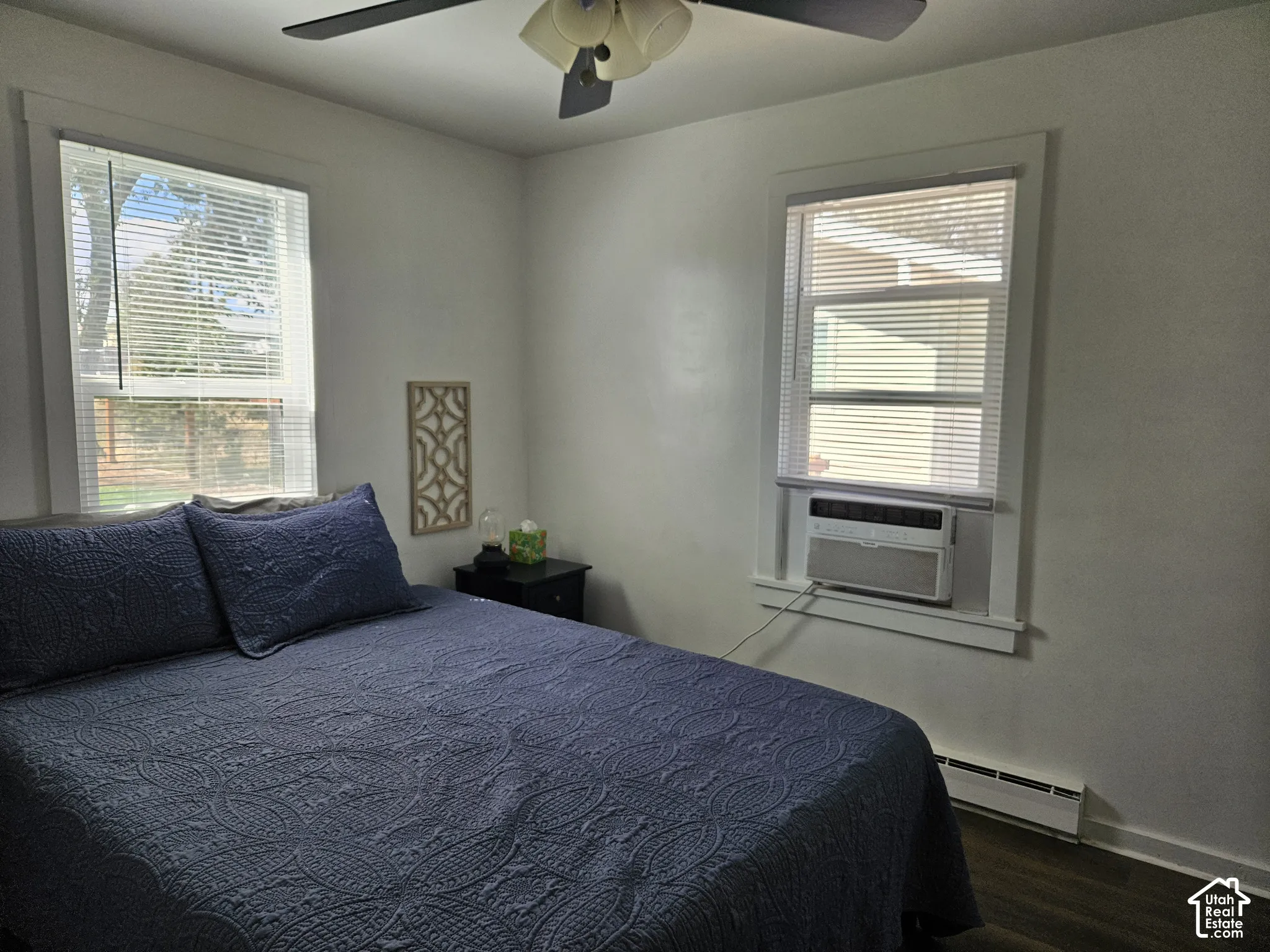 Room featuring wood-finish LVP flooring, two windows with horizontal blinds, and an integrated ceiling fan with light fixture and Window AC Unit.