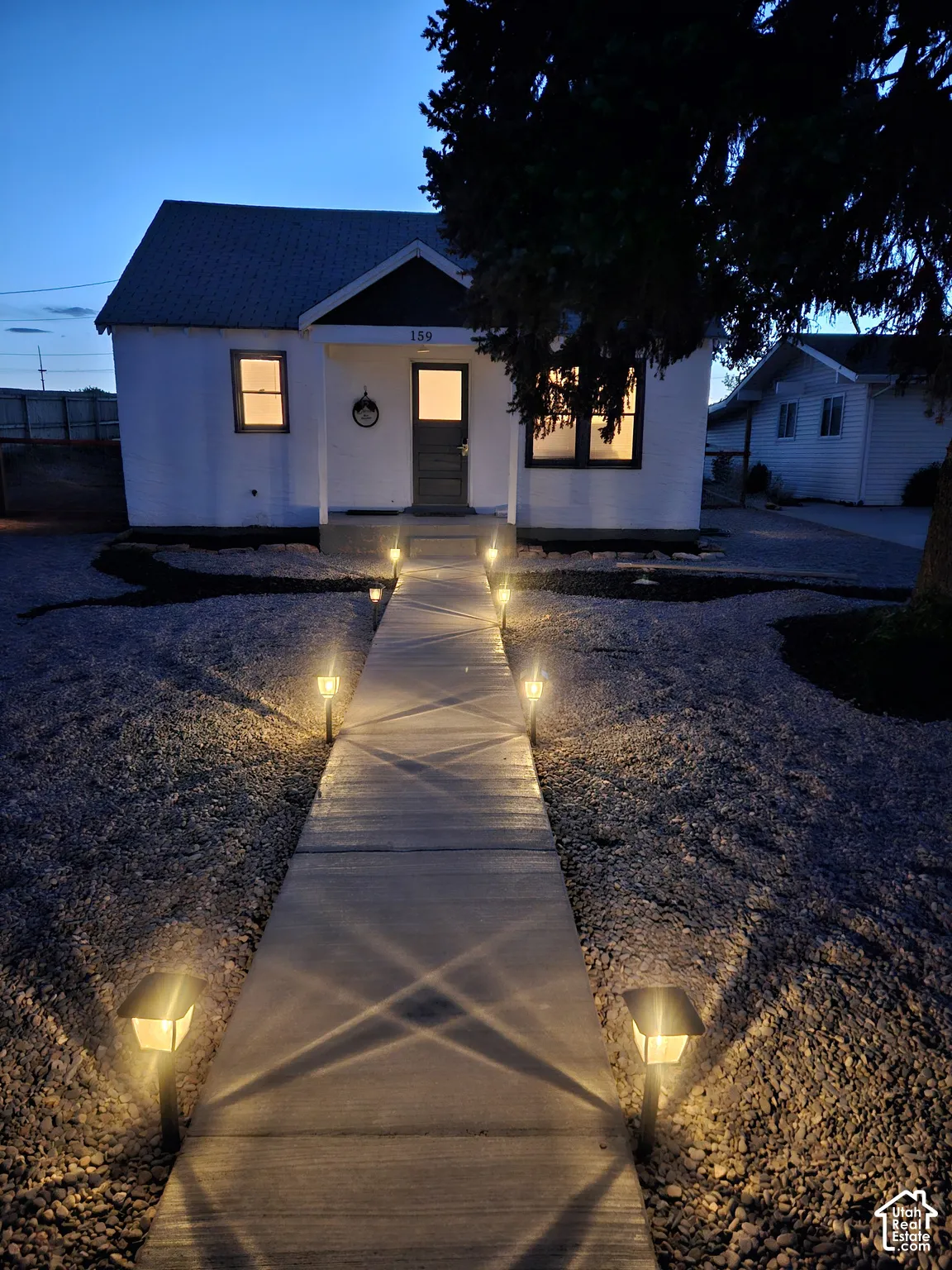 Exterior facade with light-colored siding, concrete walkway, and integrated low-voltage path lighting.